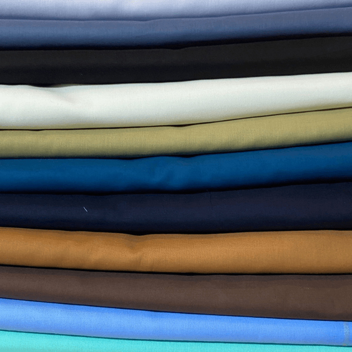 Stack of Pasha Soft Cotton men's suiting fabrics in blue, slate, black, cream, khaki, teal, navy, ochre and brown